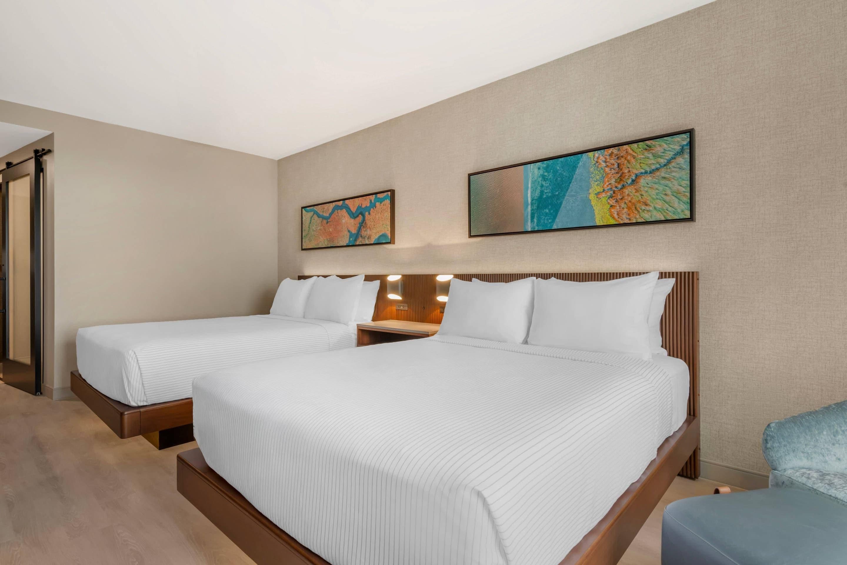 Ett hotellrum med två sängar, en sänggavel i trä och två tavlor som hänger på väggen.