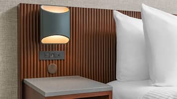A modern bedroom with a wooden headboard, a bedside table, a lamp, and a white pillow.
