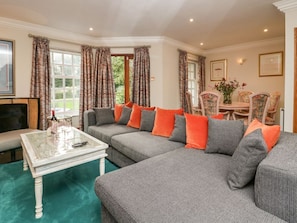 A living room with a sectional sofa, a glass coffee table, and a dining area with a table and chairs. - Lakeside View, Windermere Lake (Ulverston)