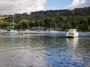 Ein ruhiger See mit Booten, einer Anlegestelle und einem bewaldeten Hügel im Hintergrund.