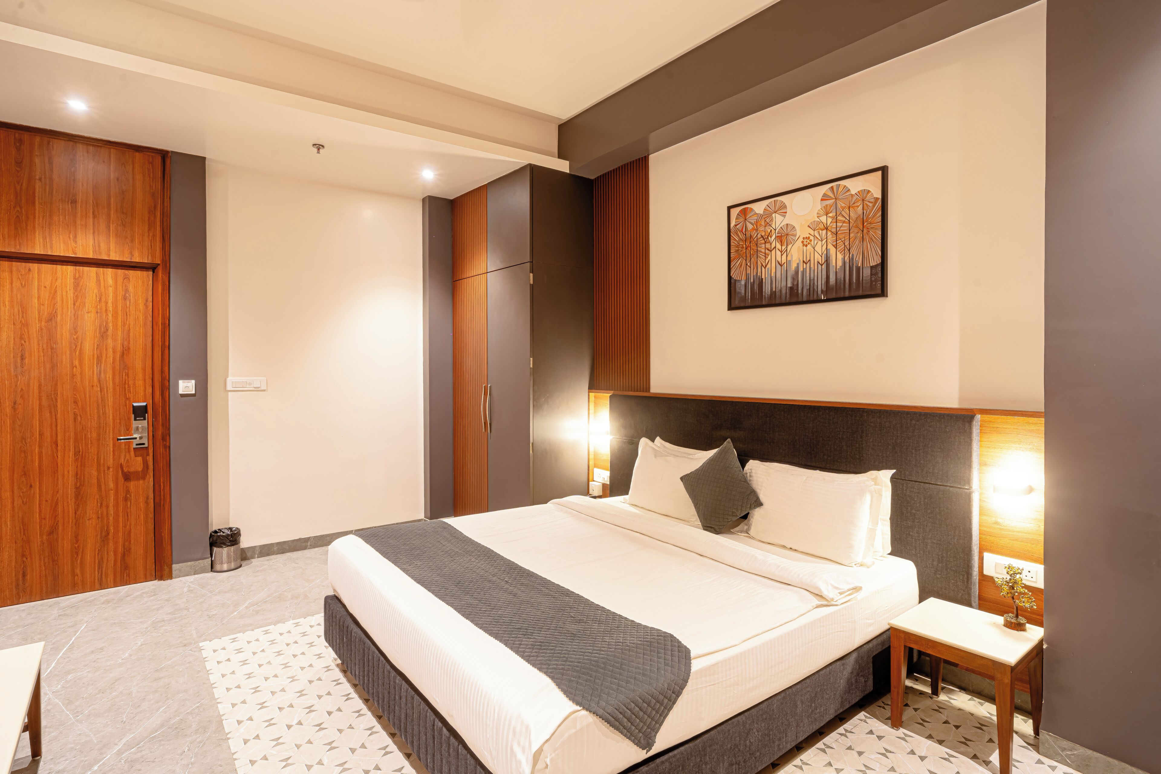 A hotel room with a large bed, bedside table, and a wall-mounted artwork.