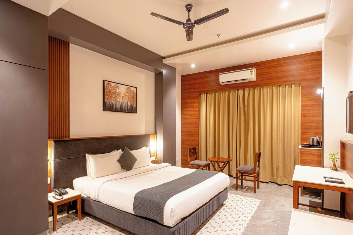 Une chambre d’hôtel comprenant un lit, une table de chevet, une commode, un bureau, une chaise et un ventilateur de plafond.
