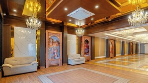 A spacious lobby with chandeliers, a marble wall, and a patterned rug.