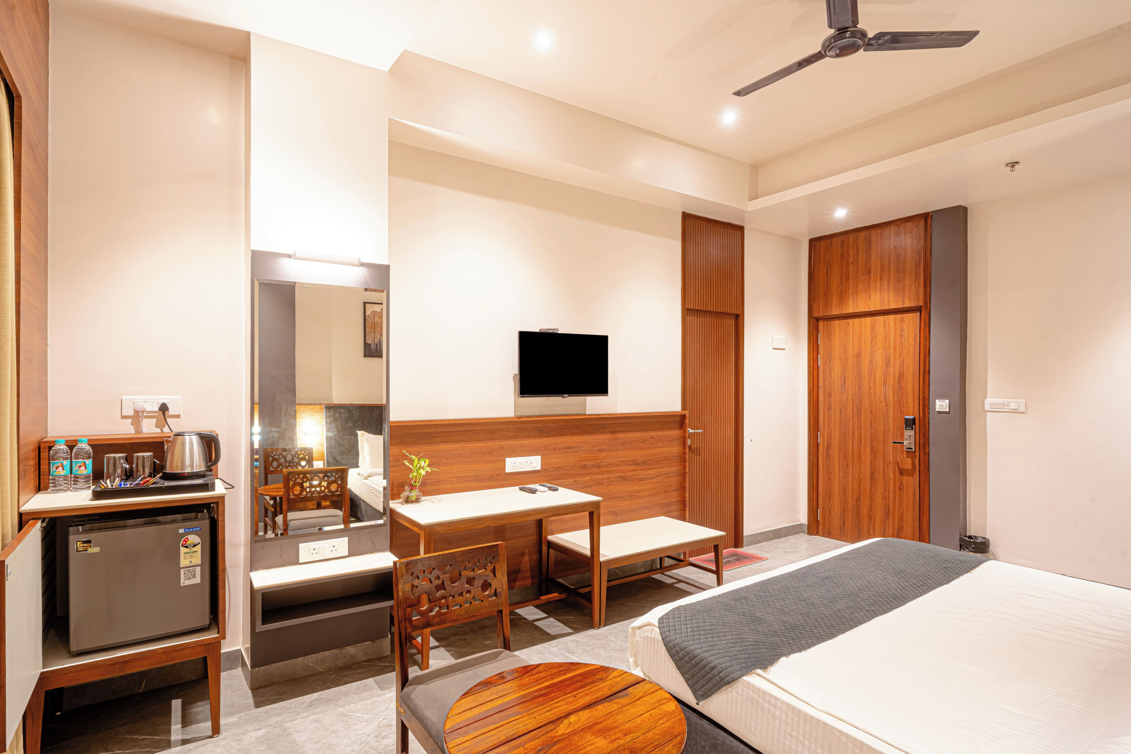 A hotel room with a bed, a desk, a chair, a small refrigerator, a television, and a wardrobe.