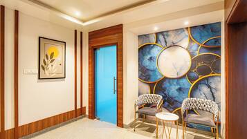 Un vestíbulo de hotel con una puerta azul, una obra de arte enmarcada, una pared de mármol con diseños circulares y dos sillones estampados.