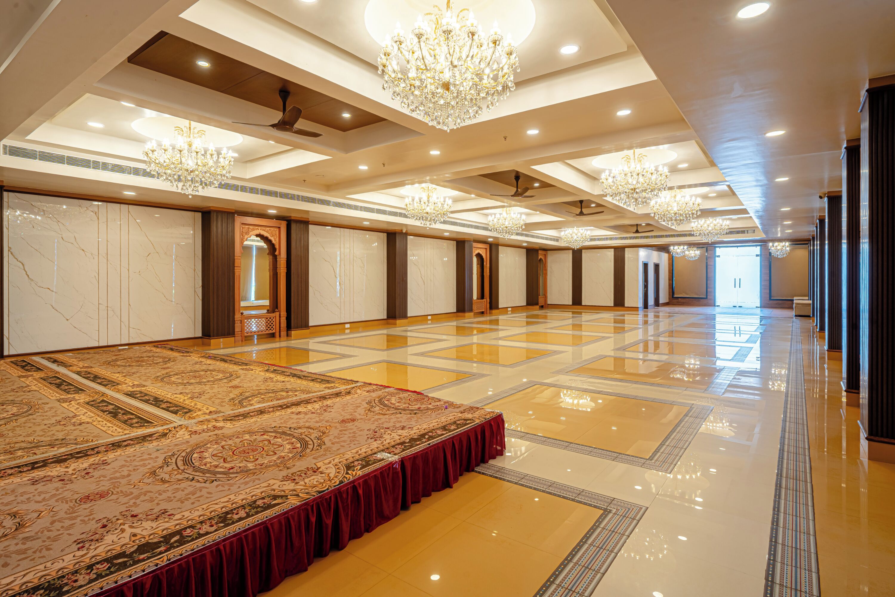 Amplia habitación de hotel con un gran suelo alfombrado, varios candelabros y piso pulido.