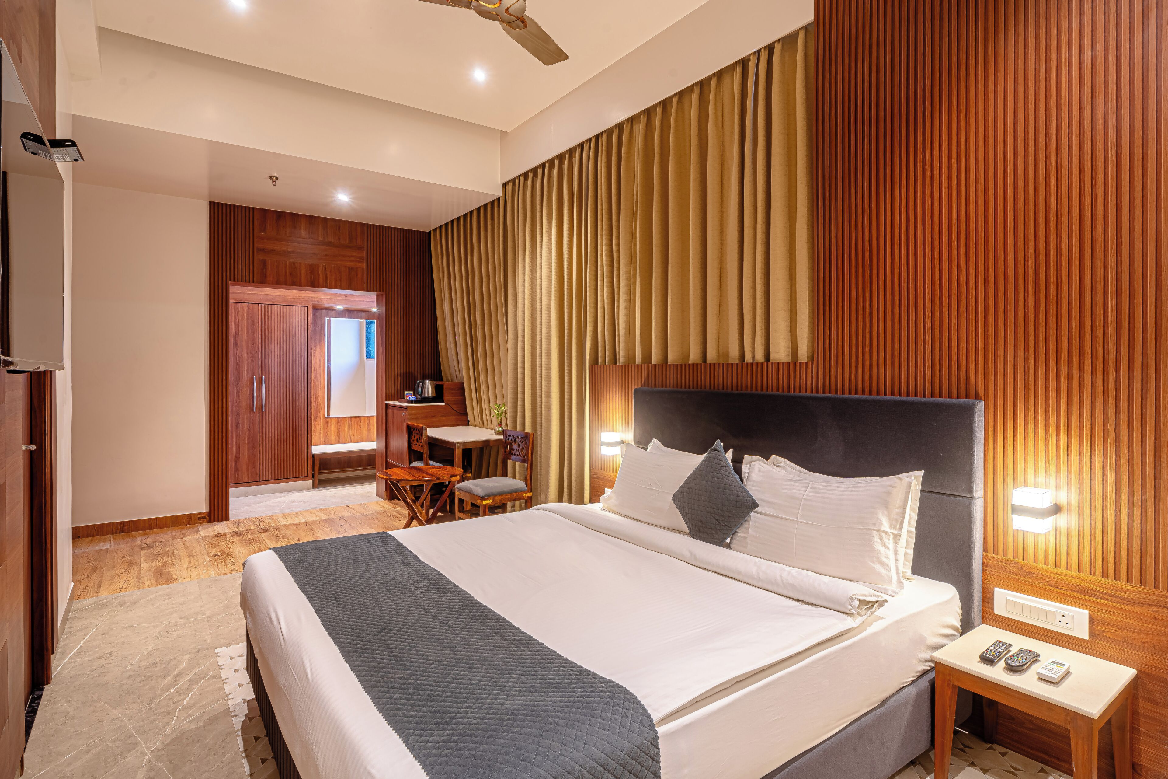 Ein Hotelzimmer mit einem großen Bett, einem Schreibtisch mit Stuhl, einem kleinen Tisch und einem Deckenventilator.