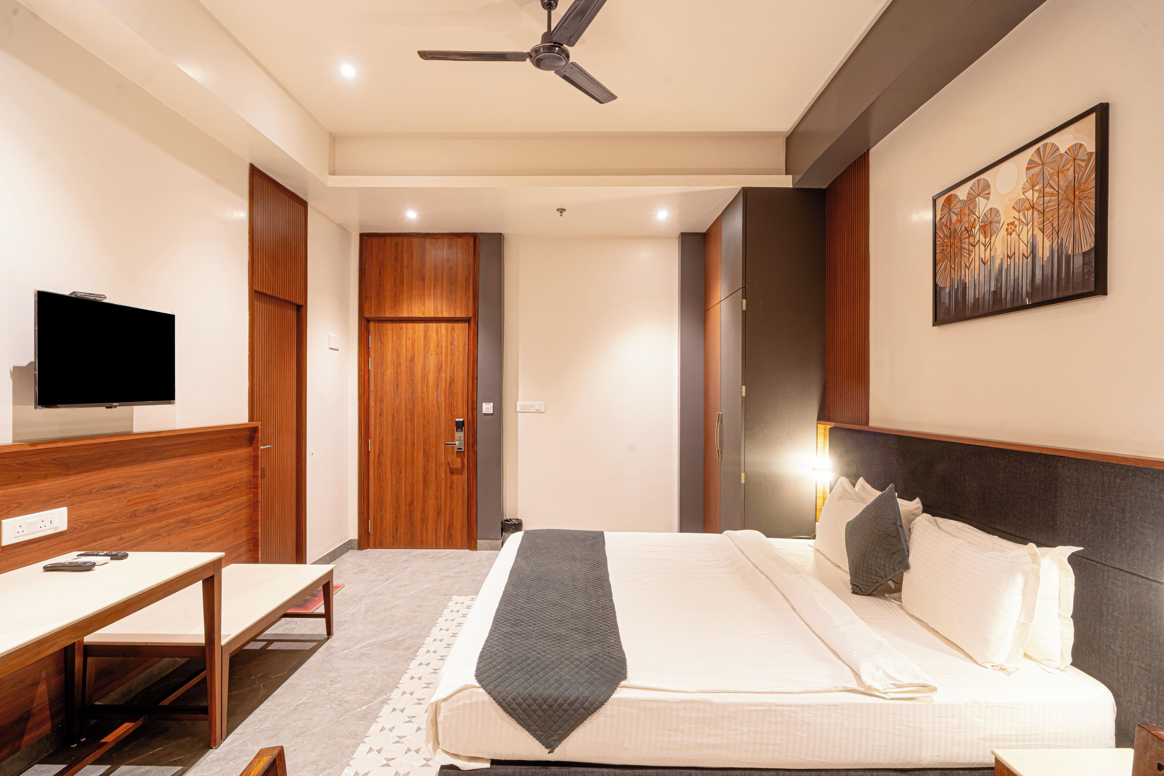 A hotel room with a bed, a desk, a television, and a ceiling fan.