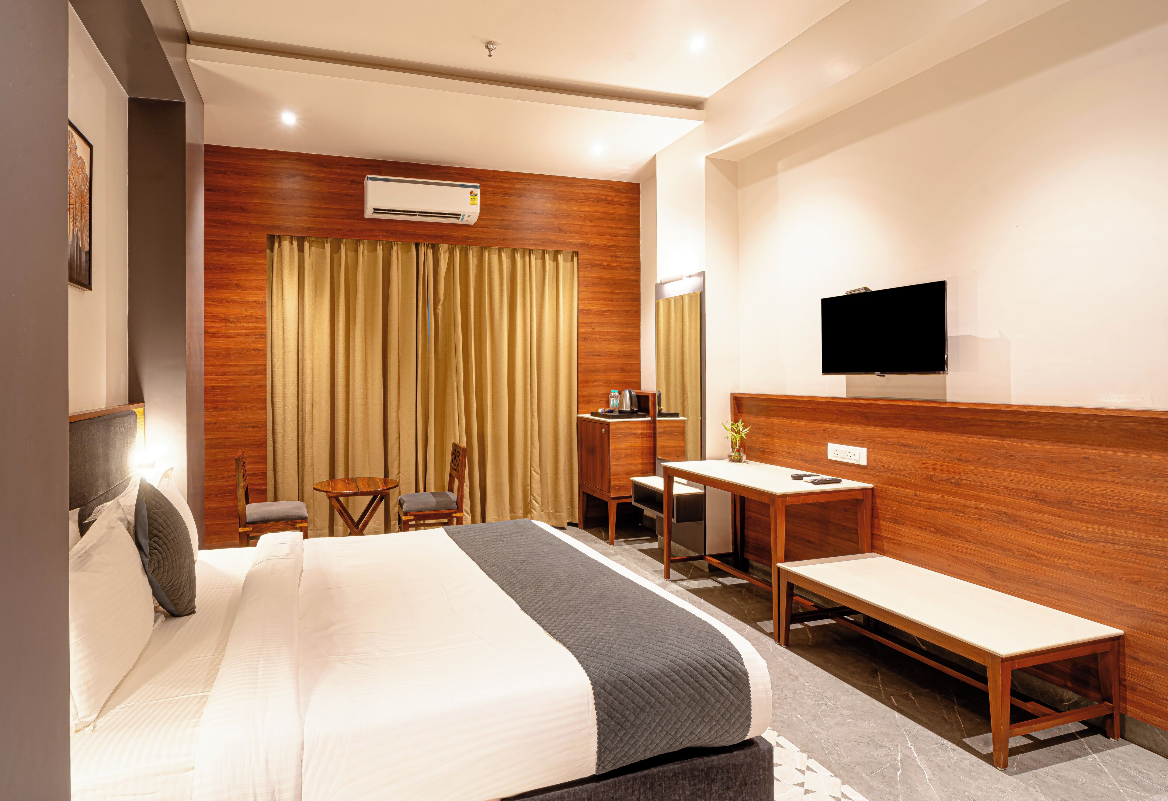 A hotel room with a bed, a desk, a chair, a television, and an air conditioning unit.
