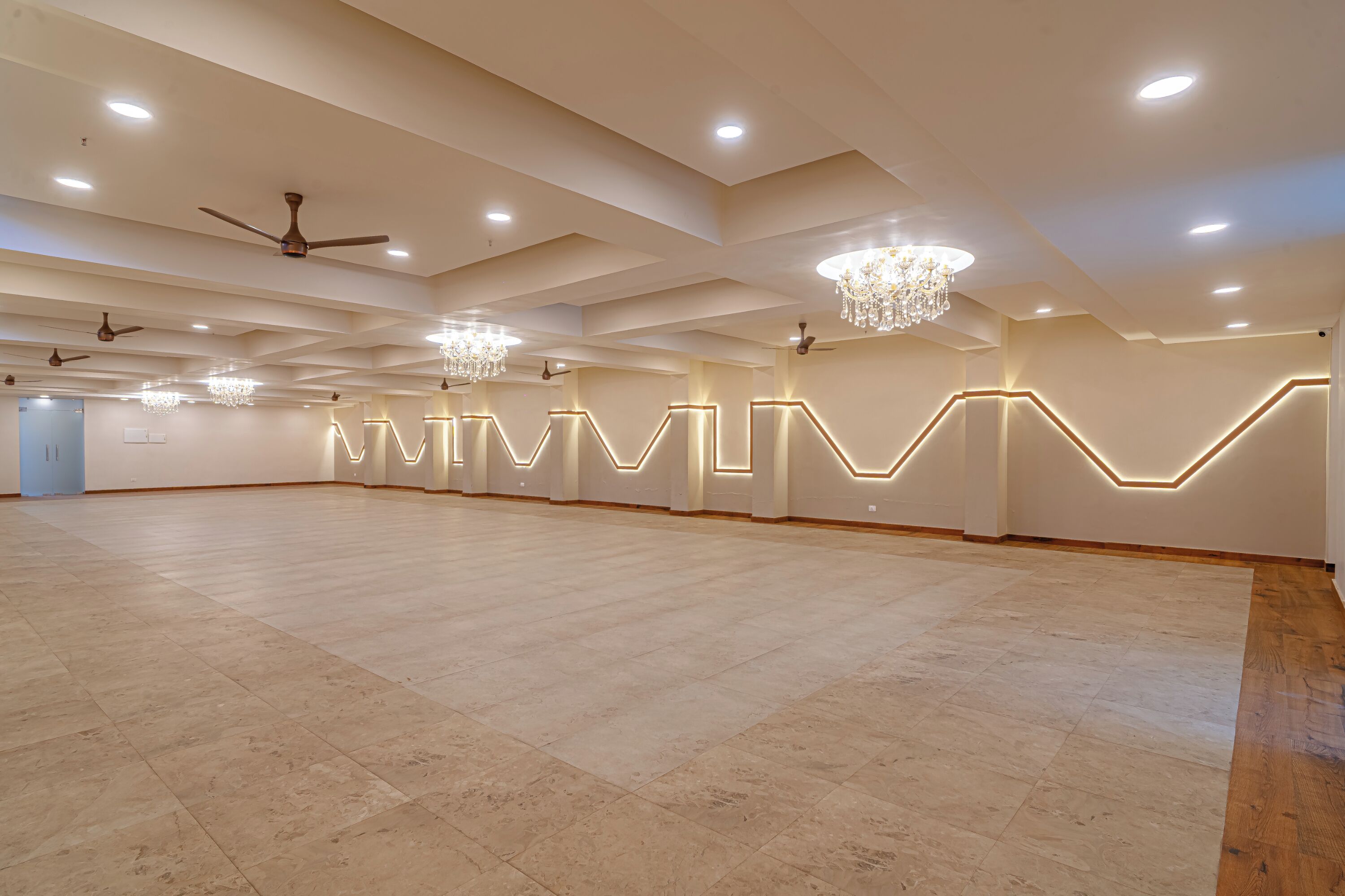 A spacious hall with a high ceiling, recessed lighting, chandeliers, and ceiling fans.