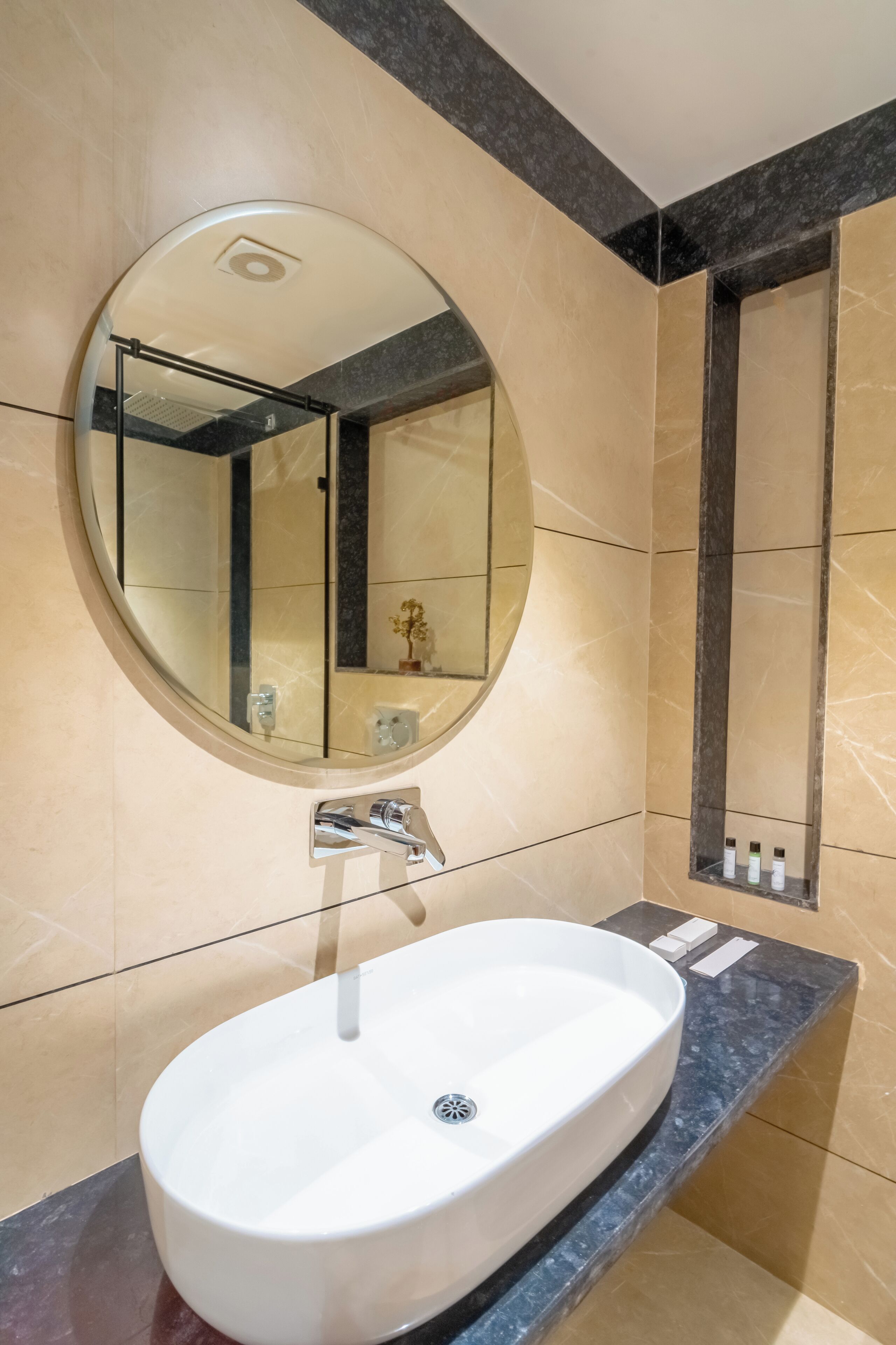 A bathroom with a round mirror, a white sink, and a marble-tiled wall.