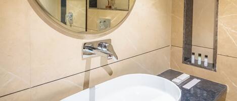 A bathroom with a round mirror, a white sink, and a marble-tiled wall.