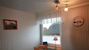 Ett rum med en randig vägg, ett fönster med utsikt, en klocka och ett bord med en rutig duk.