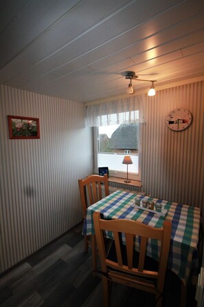 A room with a striped wall, a window with a view, a clock, and a table with a checkered tablecloth. - Pidder Lyng - FW 4 - Holiday apartment Pidder Lyng FW 4 - close to the beach, with WLAN & (Utersum)