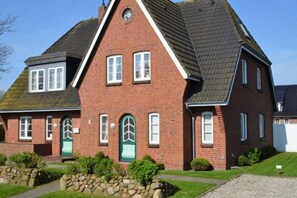 A red brick house with a gabled roof, a front entrance with a green door, and a stone pathway leading to the front. - House Süüderwoi - apartment 3 - ground floor - vacation apartment in Borgsum: terrace, garden, (Borgsum)