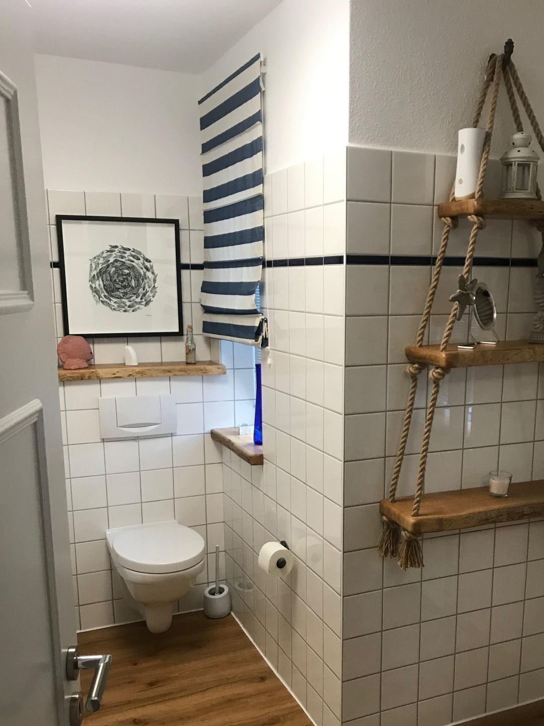 Een badkamer met een toilet, een handdoekhouder, een kunstwerk in een lijst en een plank met een kaars en een klein potje.