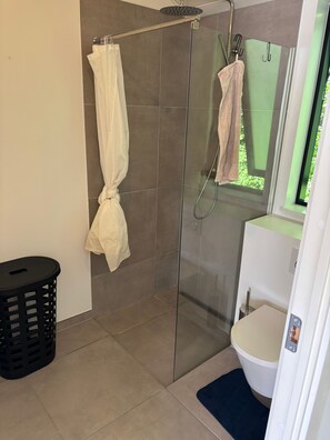 A modern bathroom with a glass shower enclosure, a white toilet, and a small black trash bin. - Stylish Cottage Near Beach, Cliff and Harbour Life (Rodvig Stevns)