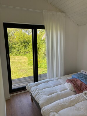A bedroom with a bed, a window with curtains, and a view of greenery outside. - Stylish Cottage Near Beach, Cliff and Harbour Life (Rodvig Stevns)