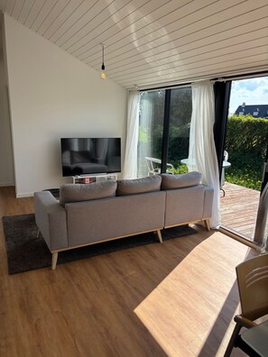A modern living room with a sofa, TV, and a view of the outdoors. - Stylish Cottage Near Beach, Cliff and Harbour Life (Rodvig Stevns)