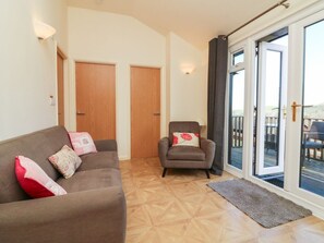Un salon comprenant un canapé, un fauteuil et une grande porte-fenêtre coulissante donnant sur un espace extérieur.