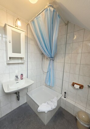 A bathroom with a bathtub, a sink, a mirror, and a shower curtain. - Promenadenblick - Apartment 3 - Holiday apartment with balcony and extraordinary (Wyk auf Föhr)