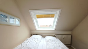 A bedroom with a skylight, a bed with white linens, a radiator, and a framed picture on the wall. - Promenadenblick - Apartment 3 - Holiday apartment with balcony and extraordinary (Wyk auf Föhr)