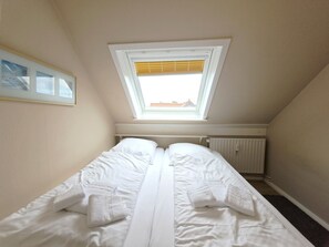 A bedroom with a skylight, a bed with white linens, a radiator, and a framed picture on the wall. - Promenadenblick - Apartment 3 - Holiday apartment with balcony and extraordinary (Wyk auf Föhr)