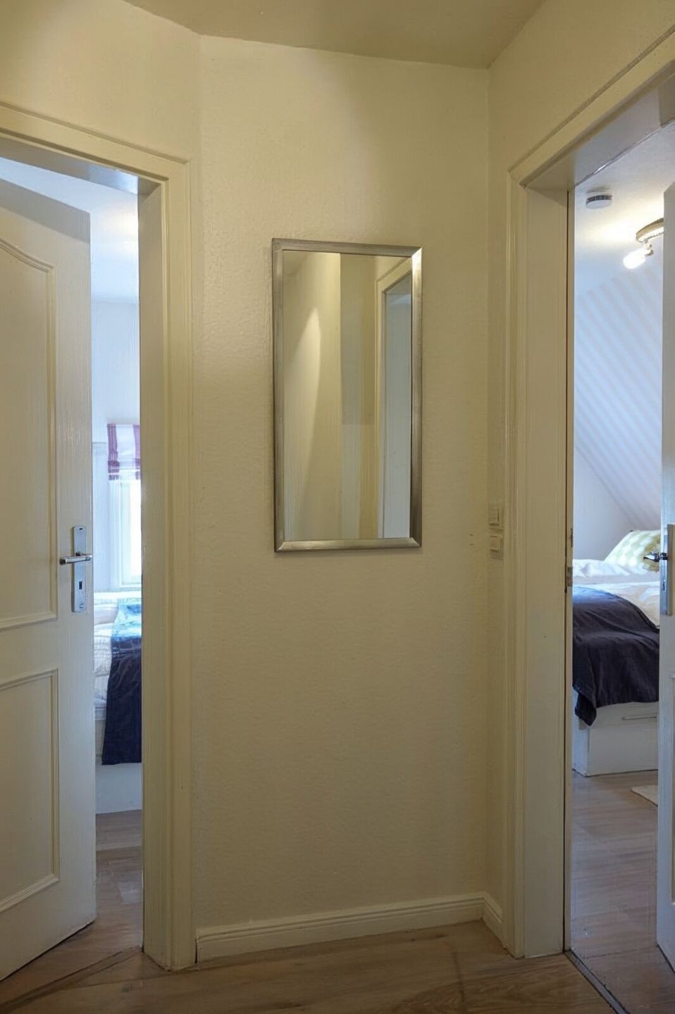 Een gang met een spiegel aan de muur, houten vloeren en een deur naar een slaapkamer.