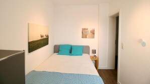 Ein Schlafzimmer mit einem Bett, zwei Kissen, einem Nachttisch, einer Lampe und zwei Wandbildern.