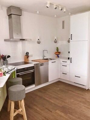 Una cocina moderna con armarios blancos, una campana extractora de acero inoxidable, lavavajillas y encimera de madera.