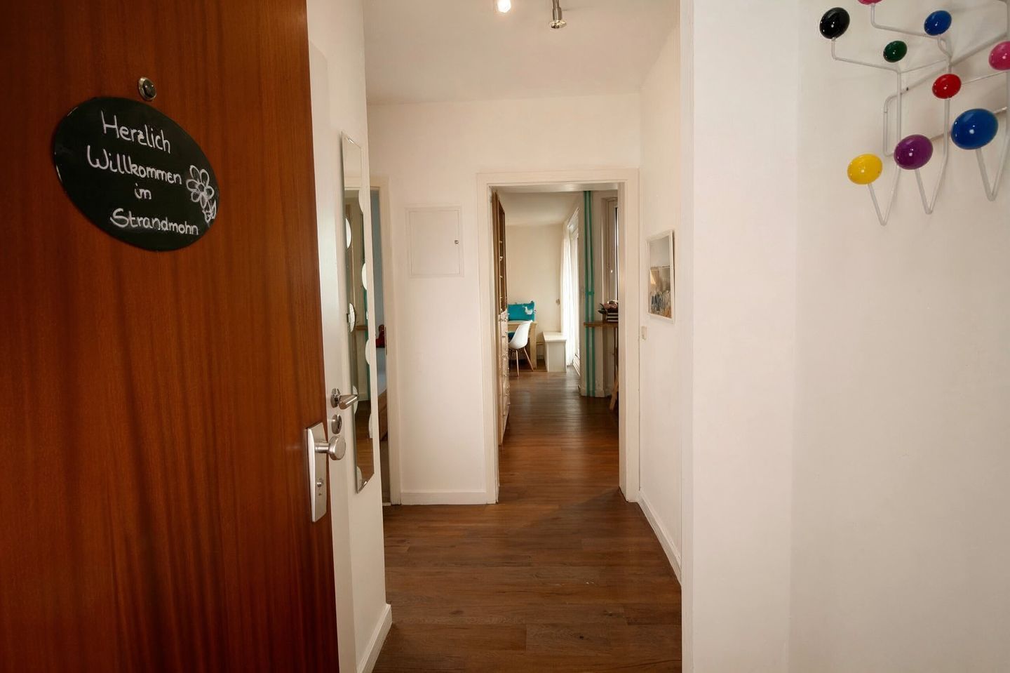 Un pasillo con una puerta de madera, un cartel de bienvenida y una decoración de pared colorida.