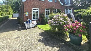 A two-story brick house with a sloped roof, a paved driveway, and a garden with pink flowers. - Austernfischer - Holiday apartment Austernfischer in Wyk auf Föhr - close to the beach with (Wyk auf Föhr)