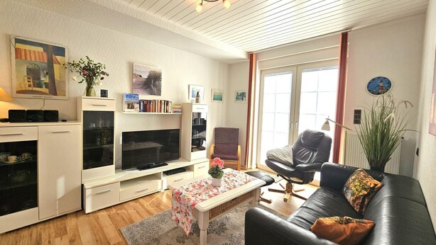 A living room with a flat-screen TV, a sofa, a coffee table, and a bookshelf. - Austernfischer - Holiday apartment Austernfischer in Wyk auf Föhr - close to the beach with (Wyk auf Föhr)