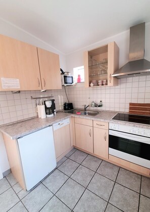 A compact kitchen with light wood cabinets, a white dishwasher, a microwave, a stove, and a sink.