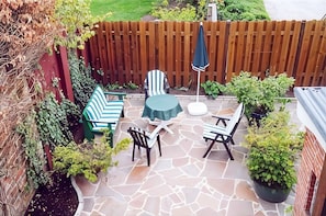 A patio with stone flooring, a table, two chairs, a striped sofa, and a wooden fence.