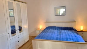 A bedroom with a bed, bedside lamps, a wardrobe, and a mirror on the wall.