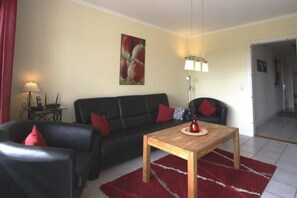 Ein Wohnzimmer mit einer schwarzen Couch, roten Kissen, einem Holztisch, einem roten Teppich, einem Gemälde an der Wand und einer Lampe.