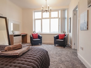 Ein Schlafzimmer mit einem großen Bett, zwei Sesseln, einem Fenster mit Aussicht, einer Chandelieber und einem Schminktisch.