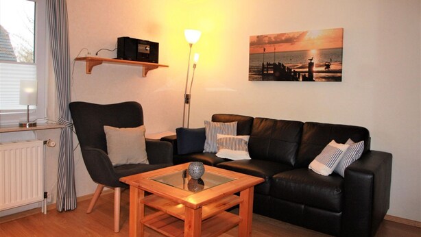 Ein Wohnzimmer mit einer schwarzen Ledersofa, einem Holztisch, einem gestreiften Sessel, einer Stehlampe und einem Sonnenuntergangsbild an der Wand.