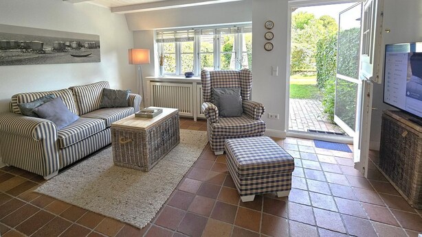 A living room with a striped sofa, a plaid armchair, a wicker ottoman, and a television on a stand. - Pastoratshof - House 6 - 5-star vacation home Pastoratshof - House 6 with sauna & sauna facilities (Wrixum auf Föhr)