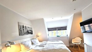 A bedroom with a bed, a chair, a window, and a painting on the wall. - Pastoratshof - House 6 - 5-star vacation home Pastoratshof - House 6 with sauna & sauna facilities (Wrixum auf Föhr)