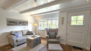 A living room with a sofa, armchair, and ottoman, a radiator, a lamp, and a door with a window. - Pastoratshof - House 6 - 5-star vacation home Pastoratshof - House 6 with sauna & sauna facilities (Wrixum auf Föhr)