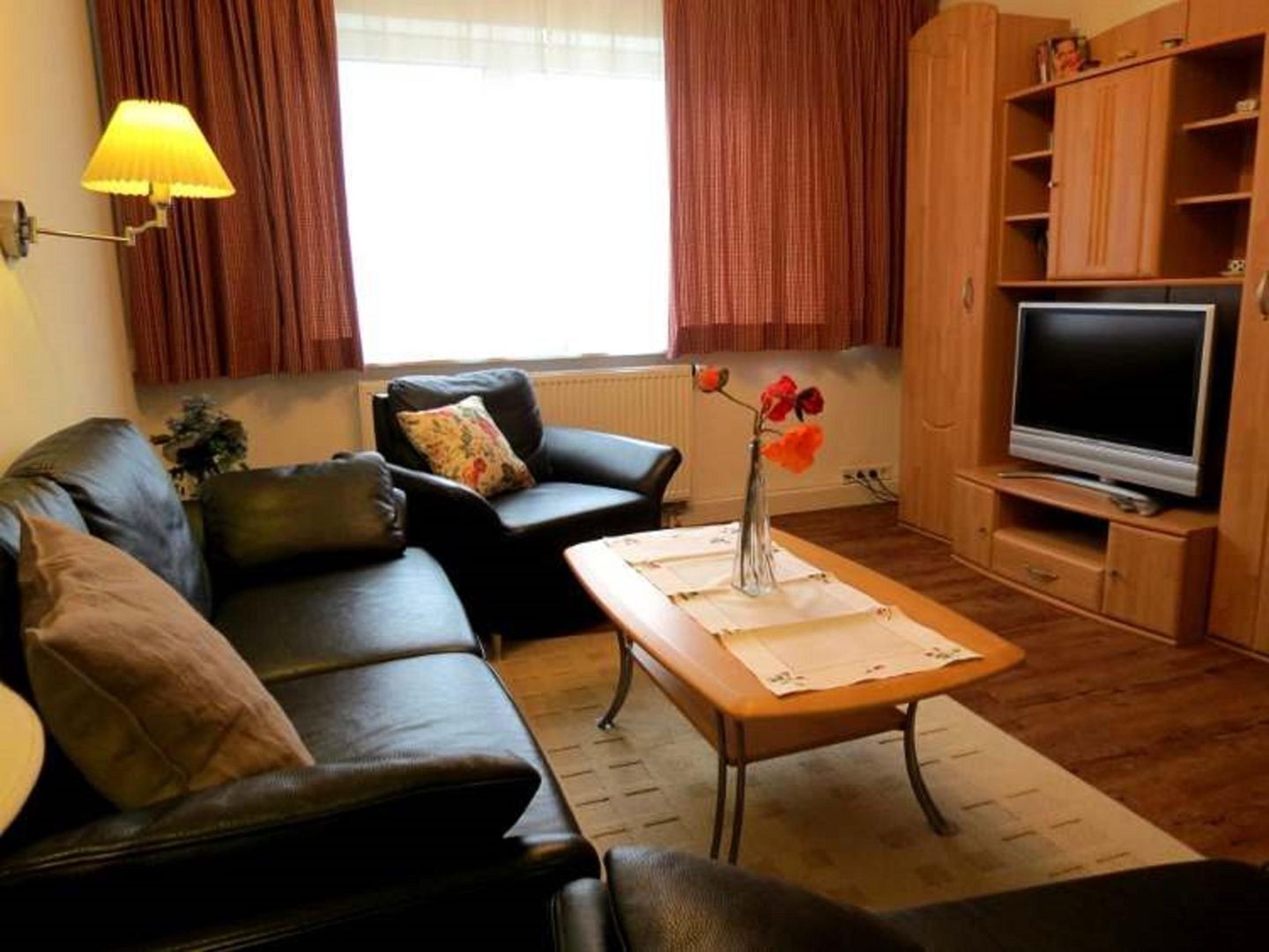 A living room with a sofa, a coffee table with a vase, a television, and wooden cabinets.