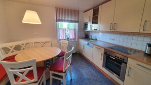 Une cuisine compacte comprenant une table à manger, des chaises, un four à micro-ondes, un four et une fenêtre avec des rideaux.
