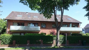 Ein zweistöckiges Backsteinhäuschen mit flachem Dach, einem Balkon im Erdgeschoss und einem kleinen Fenster im Obergeschoss.