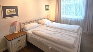 Ein Schlafzimmer mit einem Doppelbett, einem Nachttisch mit Lampe, einem gerahmten Bild an der Wand und einem Fenster mit Vorhängen.