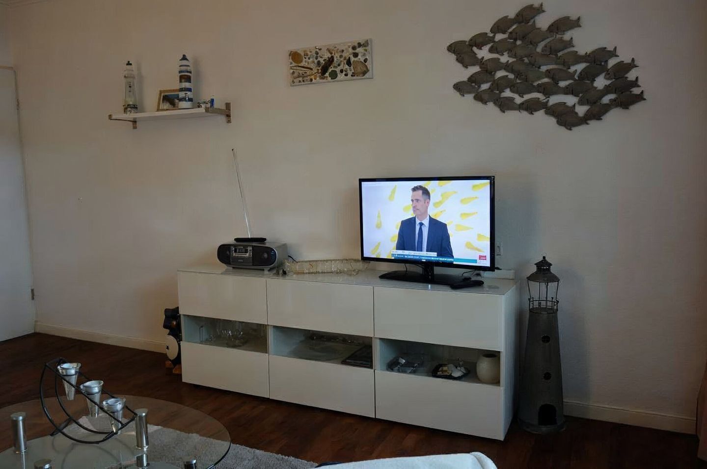 A living room with a TV, a radio, a decorative wall piece, and a tall lamp.