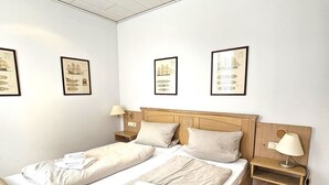 En dobbeltseng med træramme, to sengeborde med lamper og indrammede søkort på væggen.