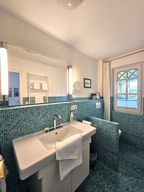 A bathroom with a white sink, a mirror, a towel rack, and a window with a view. - Palais am Südstrand - Whg. 1 - Apartment Palais am Südstrand: Sauna, (Wyk auf Föhr)