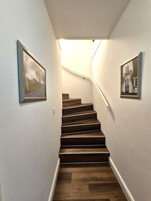 A staircase with dark wooden steps and white walls, flanked by framed pictures. - Palais am Südstrand - Apt. 1 - Palais am Südstrand Apartment: Sauna, (Wyk auf Föhr)